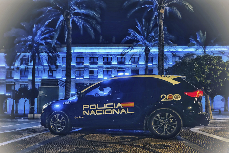 Coche de Policía Nacional frente a edificio histórico iluminado con color azul.